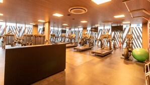 Une salle de sport équipée de divers appareils d’exercice, un comptoir d’accueil et de grandes fenêtres.