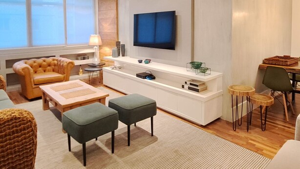 A modern living room with a sofa, coffee table, ottomans, a TV, and a dining area with chairs and a table. - Jardins Vintage I Chic 1-br Office in Jardins (São Paulo)