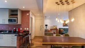 A modern kitchen with a built-in microwave, a dining area with a wooden table and green chairs, and a living room with a sofa and a coffee table. - Jardins Vintage I Chic 1-br Office in Jardins (São Paulo)