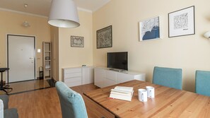 A modern living room with a wooden dining table, blue chairs, a TV, and framed cityscape pictures on the wall.