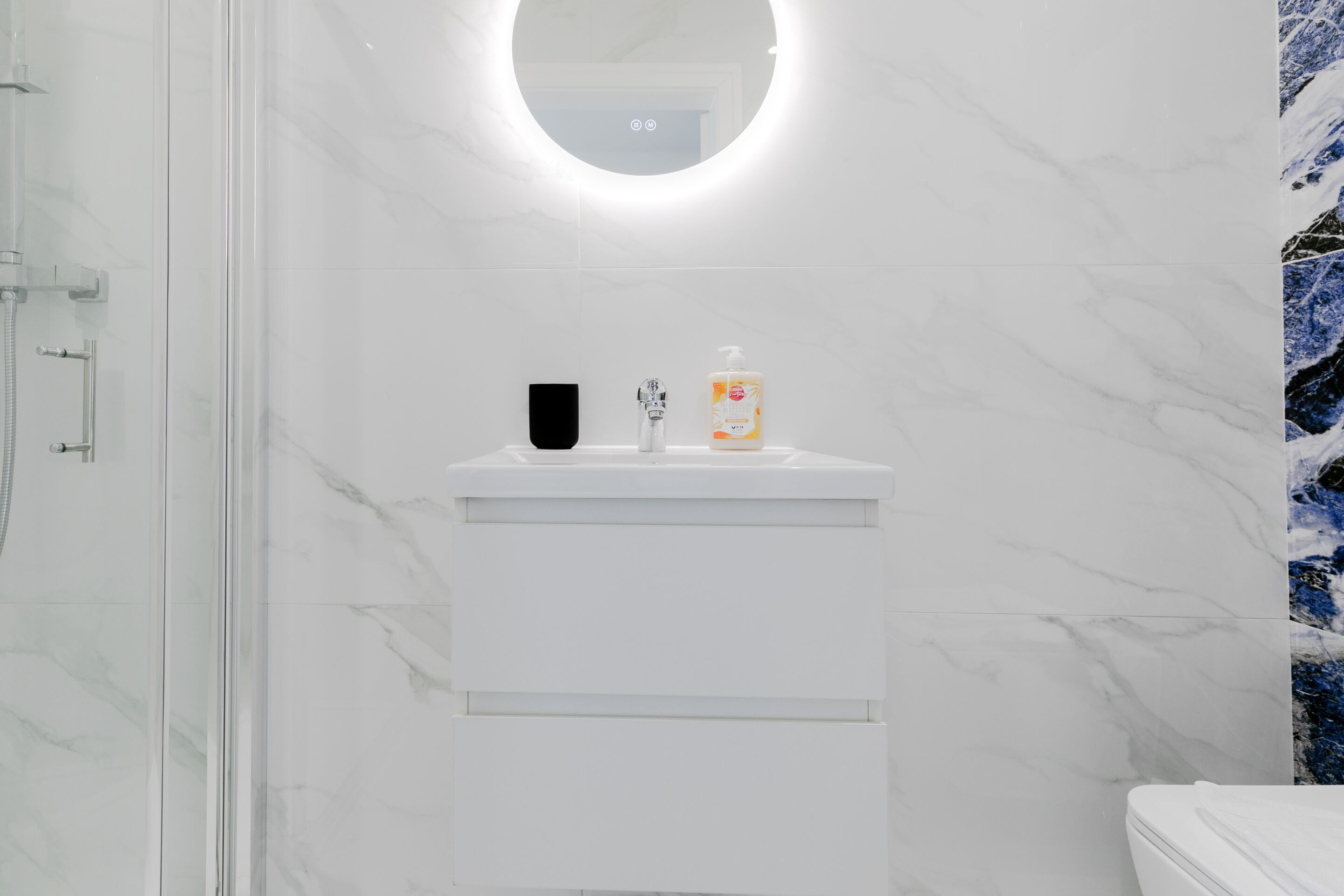 A bathroom with a white marble sink, a mirror, and a shower enclosure.
