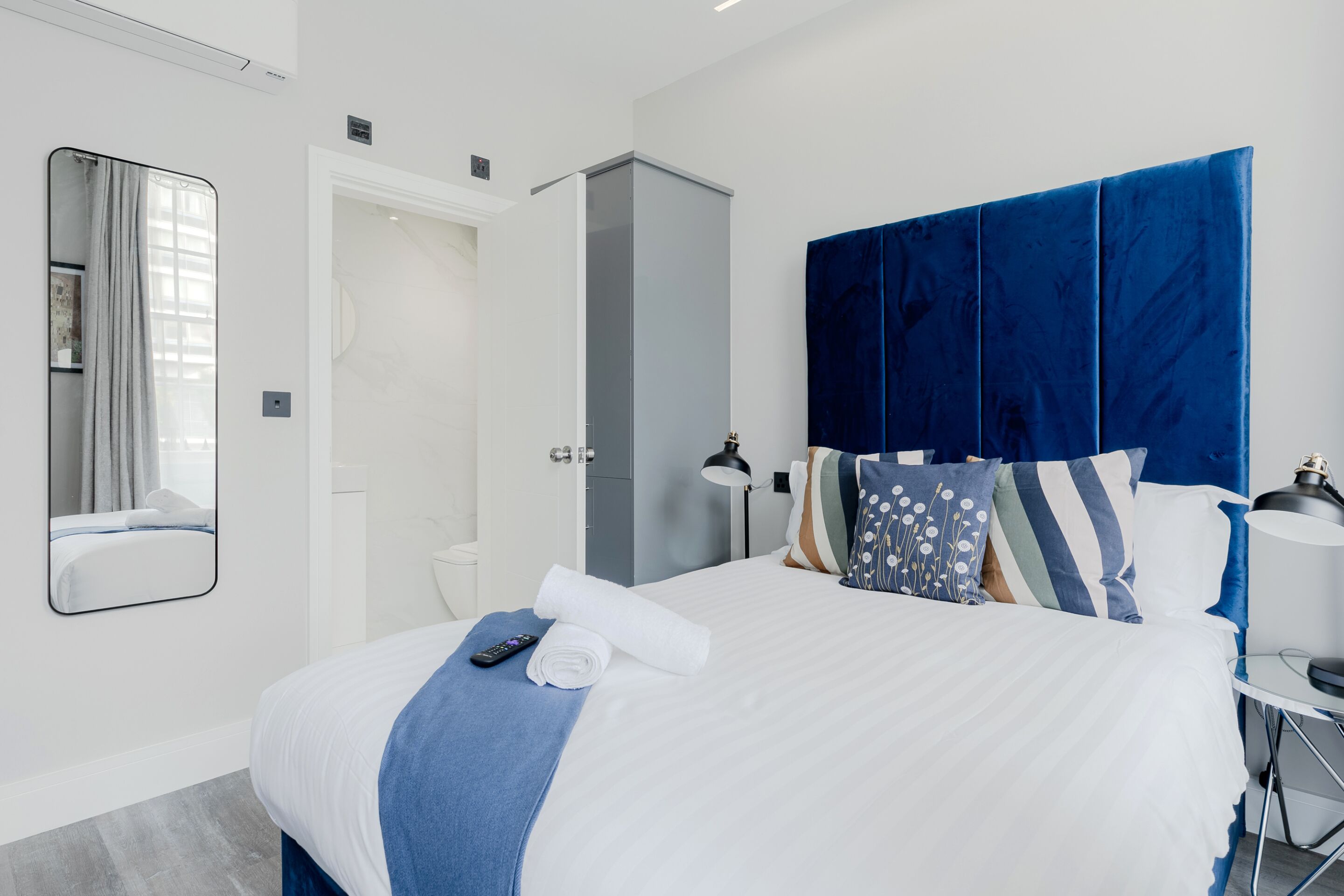 A modern hotel room with a large bed, a wardrobe, a bathroom, and a mirror.