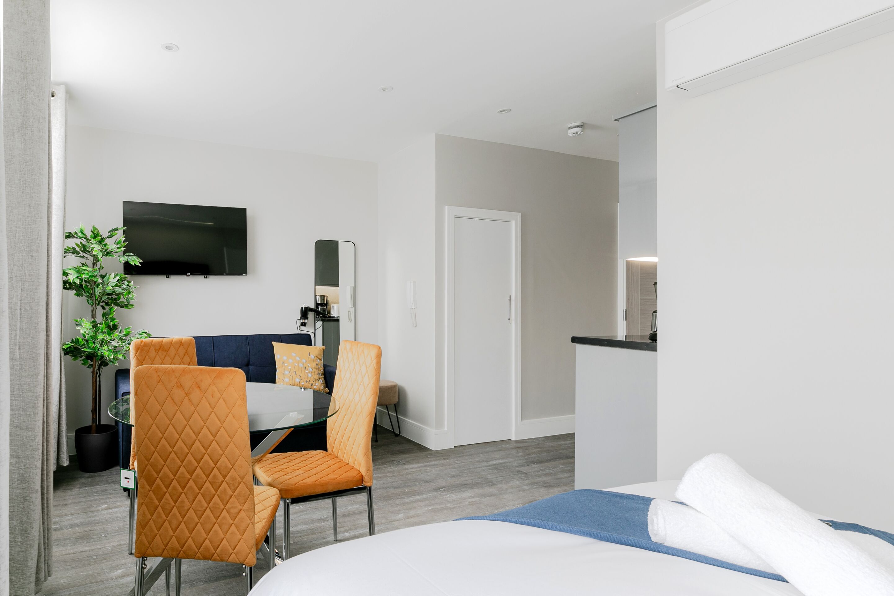 Quarto de hotel com cama, escrivaninha com cadeira, televisão e porta.