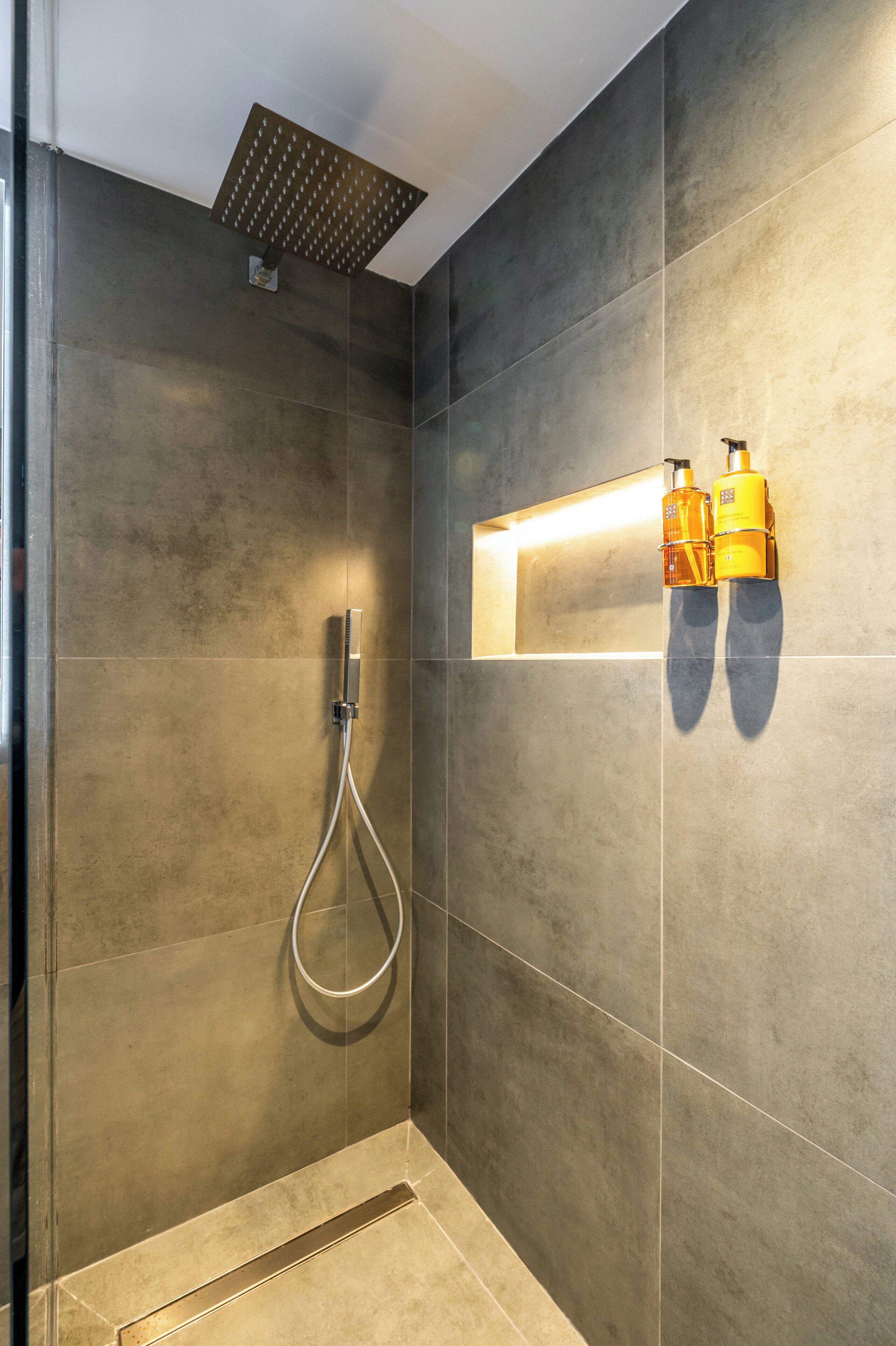Un espace douche moderne doté d’un pommeau de douche à main, d’un porte-serviettes mural et d’un luminaire rectangulaire.