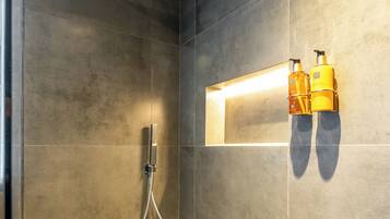 Un espace douche moderne doté d’un pommeau de douche à main, d’un porte-serviettes mural et d’un luminaire rectangulaire.