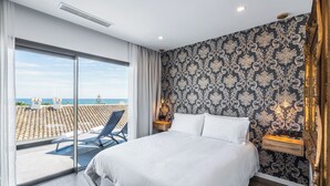 Ein Schlafzimmer mit einem großen Bett, einem Balkon mit einem Sessel und Blick aufs Meer.