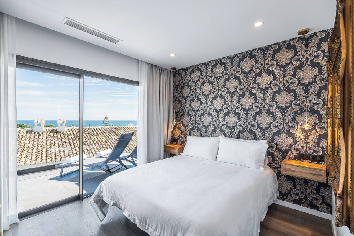 Une chambre avec un grand lit, un balcon avec une chaise et une vue sur la mer.