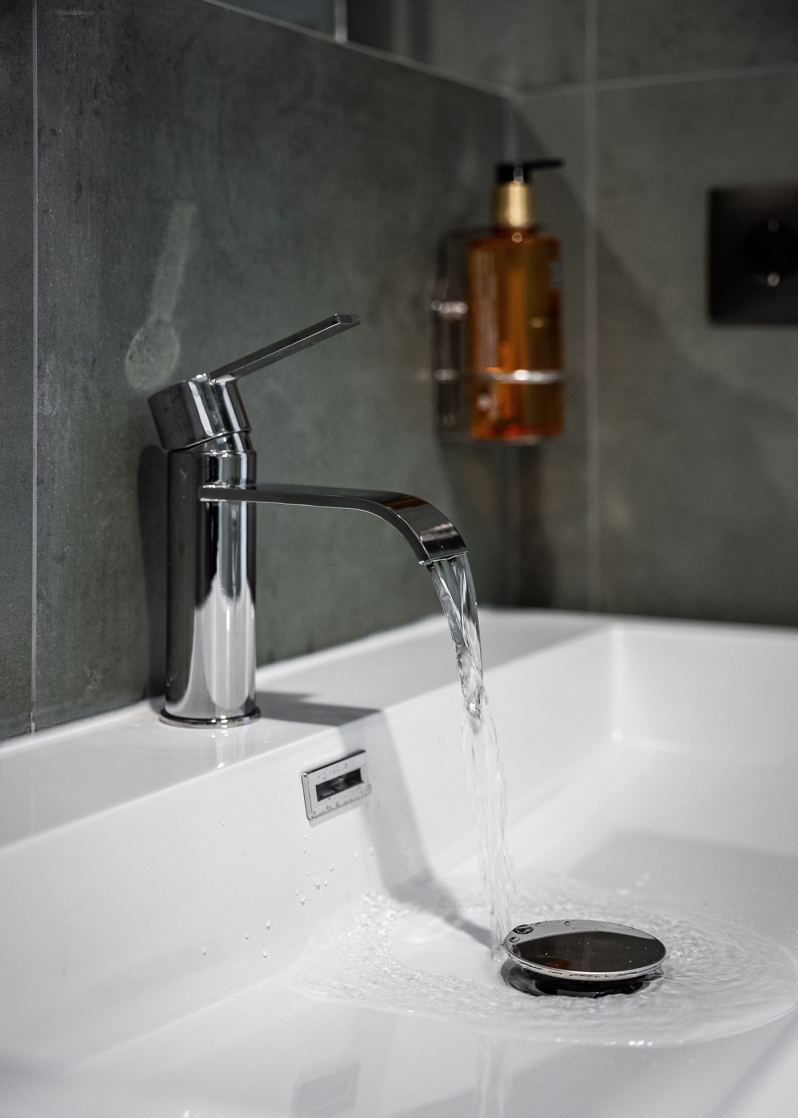 A modern bathroom with a chrome faucet and a soap dispenser on the wall.