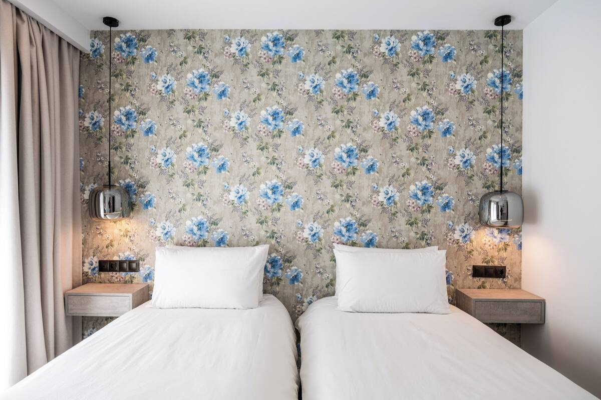 Un lit double avec une literie blanche, deux tables de chevet et un papier peint à motifs floraux.