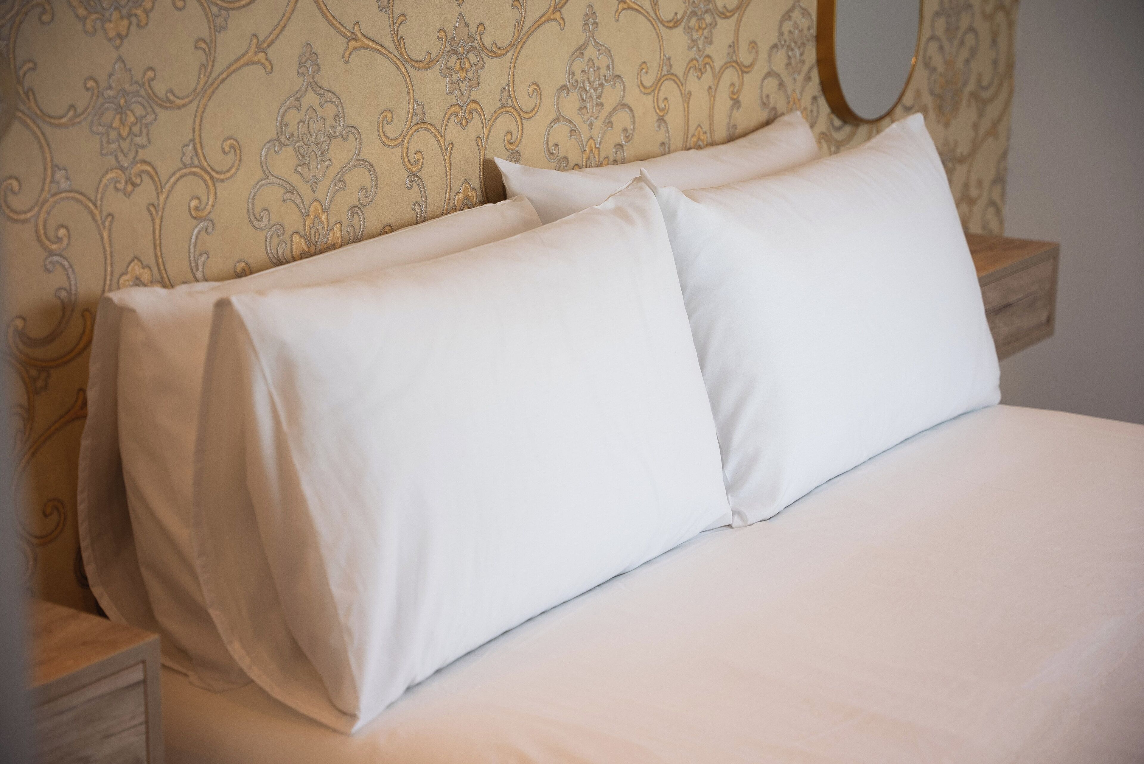 A neatly made bed with white linens and a patterned headboard.