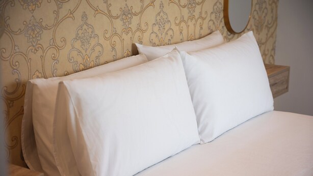 Un lit bien fait, avec du linge de lit blanc et une tête de lit à motifs.