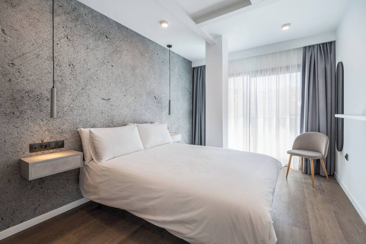 Une chambre moderne avec un grand lit, une table de chevet intégrée et un fauteuil.