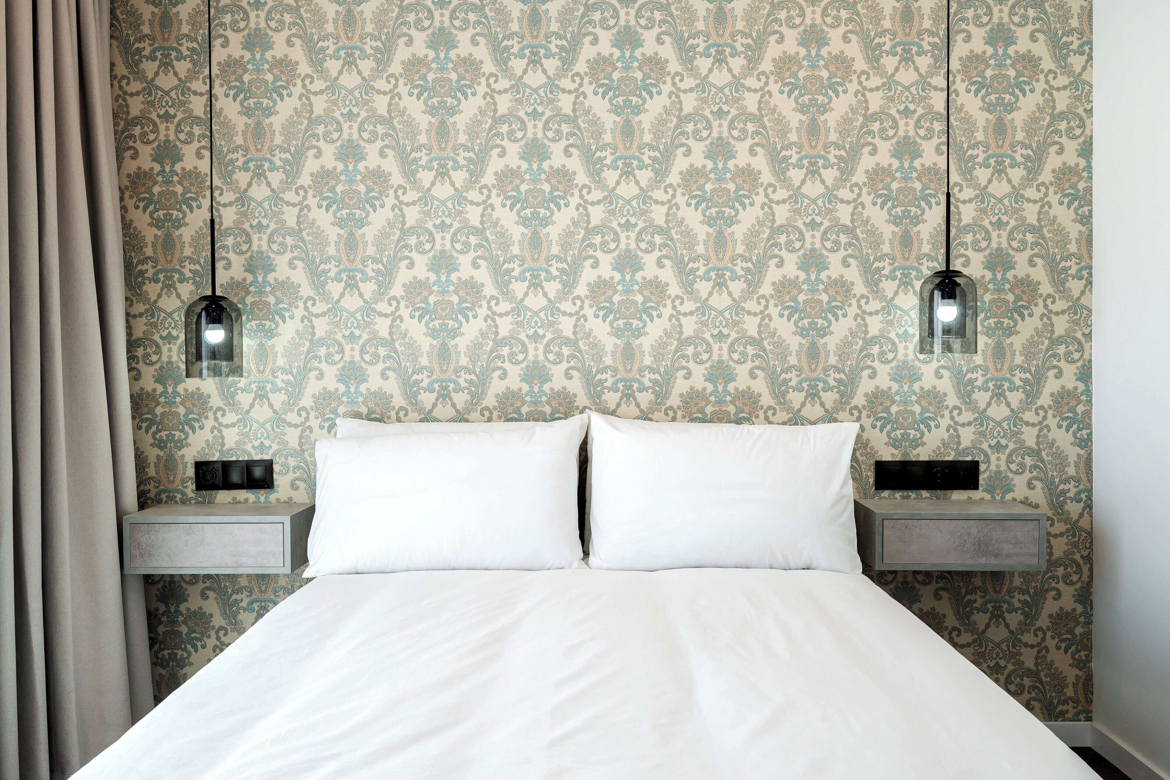 A bed with white linens, a patterned wallpaper, and two bedside tables with lamps.