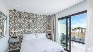 Un dormitorio moderno con una cama grande, un papel tapiz estampado, una mesita de noche, una lámpara y vistas al exterior a través de un ventanal corredera.