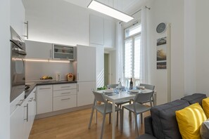 A modern kitchen with white cabinets, a dining table with chairs, and a gray sofa with yellow cushions. - Ammirato Duplex in Florence (Florence)