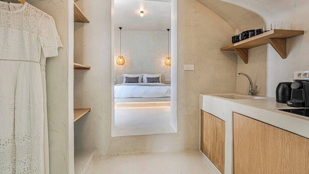 Ett modernt sovrum med en säng, sänglampor och utsikt över ett badrum med handfat och kaffemaskin.