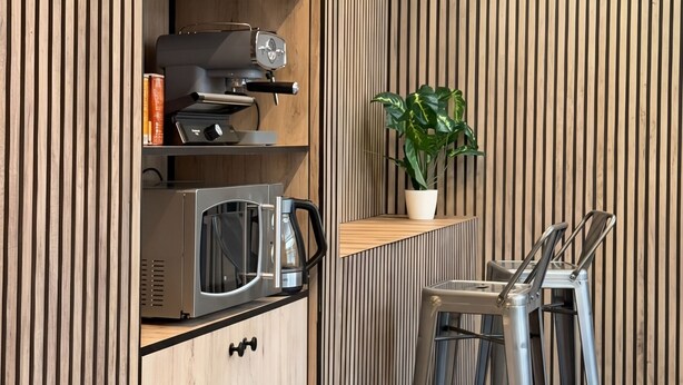 A modern kitchen with wooden cabinetry, a built-in espresso machine, a kettle, and a potted plant. - Senda Hostel Retiro (Madrid)