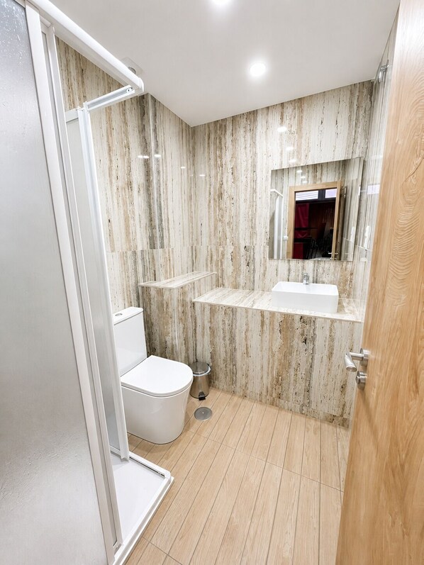 A bathroom with a shower, toilet, and vanity with a mirror.