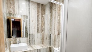 A modern bathroom with a marble wall, a white sink, a toilet, and a glass shower enclosure. - Senda Hostel Retiro (Madrid)