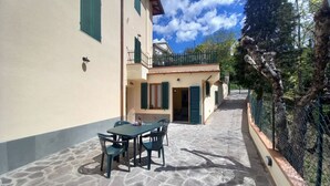 A courtyard with a stone floor, a table with chairs, and a building with green shutters and a balcony. - Lina romantic apartment Vallombrosa wifi nature (Toscana)