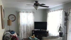 A living room with a sofa, armchair, TV, ceiling fan, and a clock on the wall. - Rest for your soul
Peace
Quiet
Nature
Secluded
Cozy


 (Lanark)