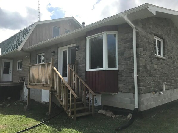 Een gelijkvloers huis met een veranda, een stenen gevel en een klein terras.