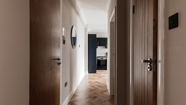 A hallway with wooden flooring and doors leading to a kitchen area. - Bright One Bedroom Flats  (London)