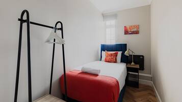 A hotel room with a bed, a nightstand, a lamp, a hanging clothes rack, and a painting on the wall.