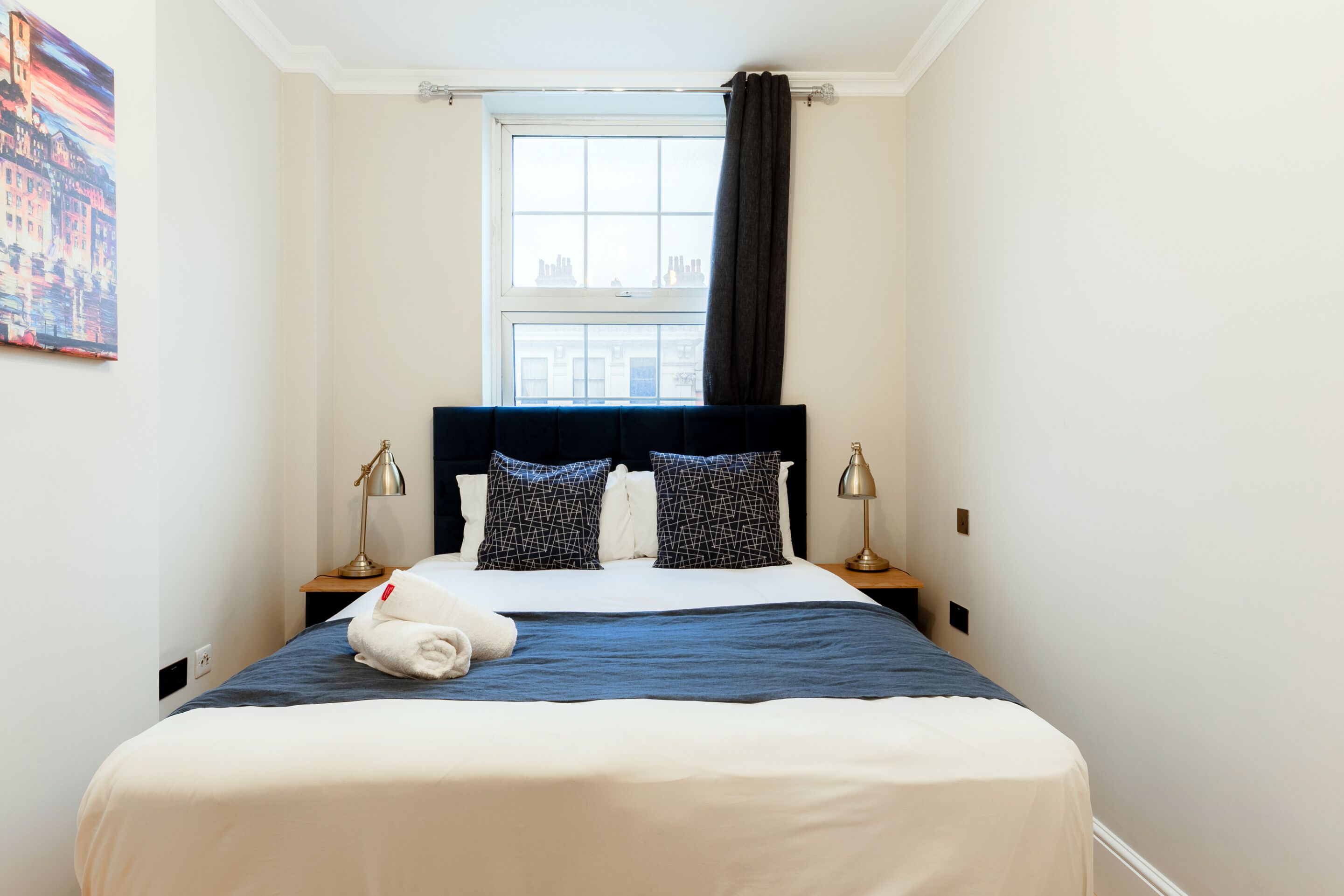 Een hotelkamer met een bed, twee bedlampen, een raam met gordijnen en een schilderij aan de muur.