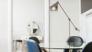 A modern room with a glass table, black chairs, a desk with a mirror, and a floor lamp. - Bright One Bedroom Flats  (London)