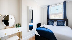 A modern hotel room with a large bed, a bedside table, a mirror, and a window with curtains. - Bright One Bedroom Flats  (London)