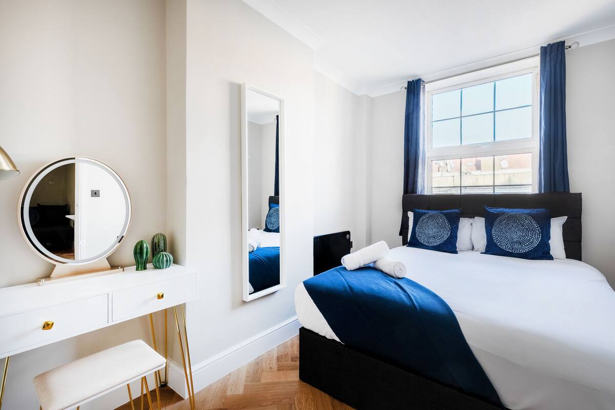 A modern hotel room with a large bed, a bedside table, a mirror, and a window with curtains.