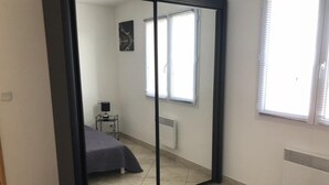 A bedroom with a bed, a small table, a mirror, and a window. - Appartement Climatisé vue Imprenable sur Mer. 2 ch. Salon Cuisine SB Terrasse (L'Île-Rousse)