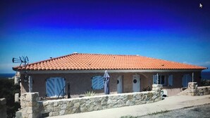A building with a red-tiled roof, stone walls, and a small porch. - Appartement Climatisé vue Imprenable sur Mer. 2 ch. Salon Cuisine SB Terrasse (L'Île-Rousse)