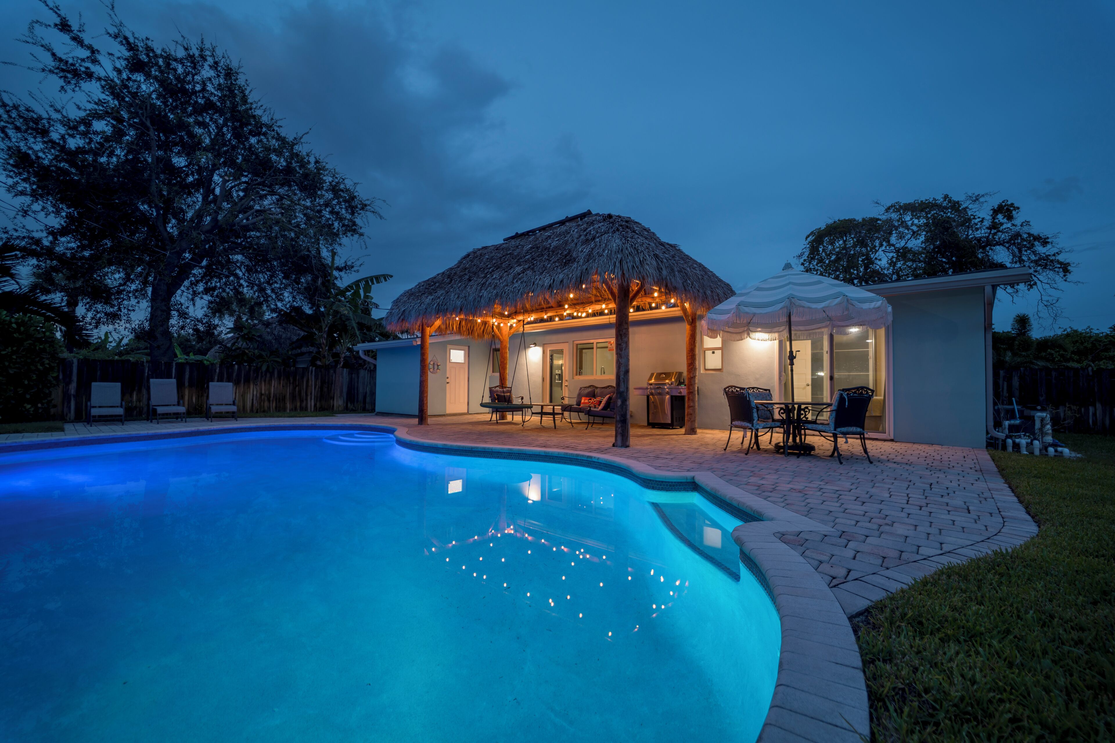 A swimming pool with a thatched-roof structure and outdoor seating.