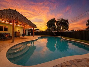 Una piscina con techo de paja, un patio con mobiliario exterior y una cerca de madera.