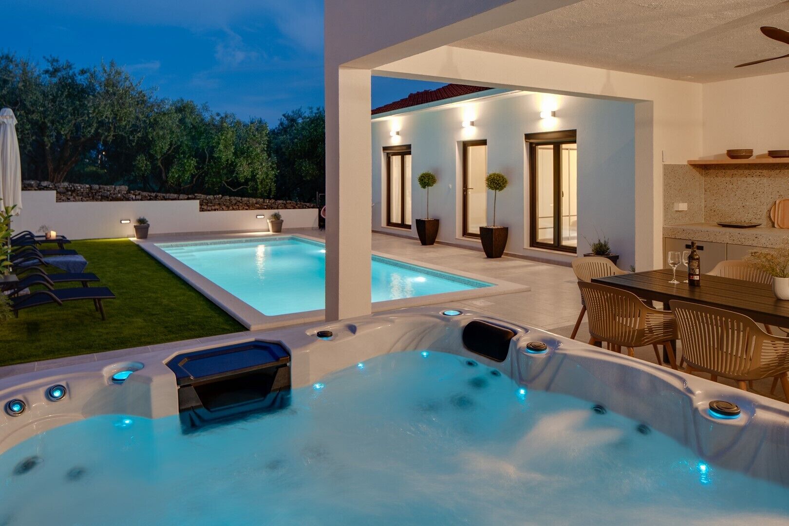 A modern outdoor pool area with hot tubs and a dining table.
