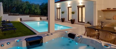 A modern outdoor pool area with hot tubs and a dining table.