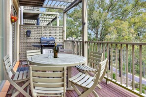 A covered outdoor patio with a round table and chairs, a grill, and a view of trees.