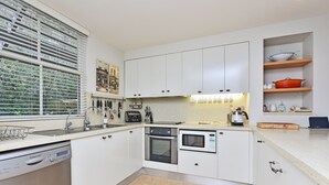 A modern kitchen with white cabinetry, a built-in oven, a microwave, and a dishwasher. - Villa 3br Gruner Veltliner located within Cypress Lakes Resort (Pokolbin)