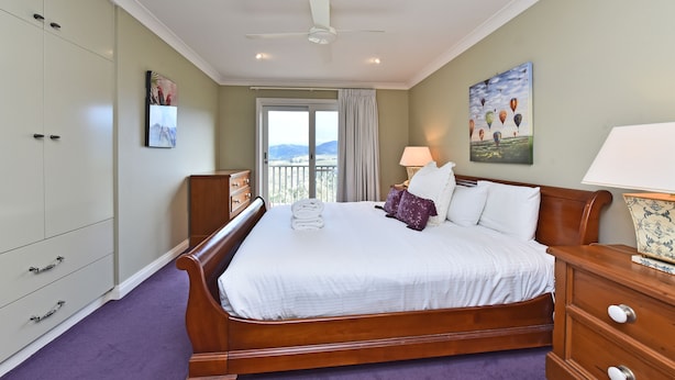 A hotel room with a large bed, a nightstand, a wardrobe, and a balcony with a view. - Villa 3br Gruner Veltliner located within Cypress Lakes Resort (Pokolbin)
