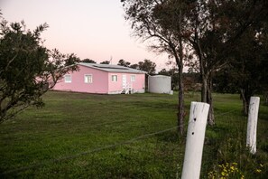 A pink house with a fenced yard and a large white building in the background.