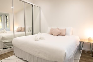 A hotel room with a large bed, a mirror, and a bedside table.