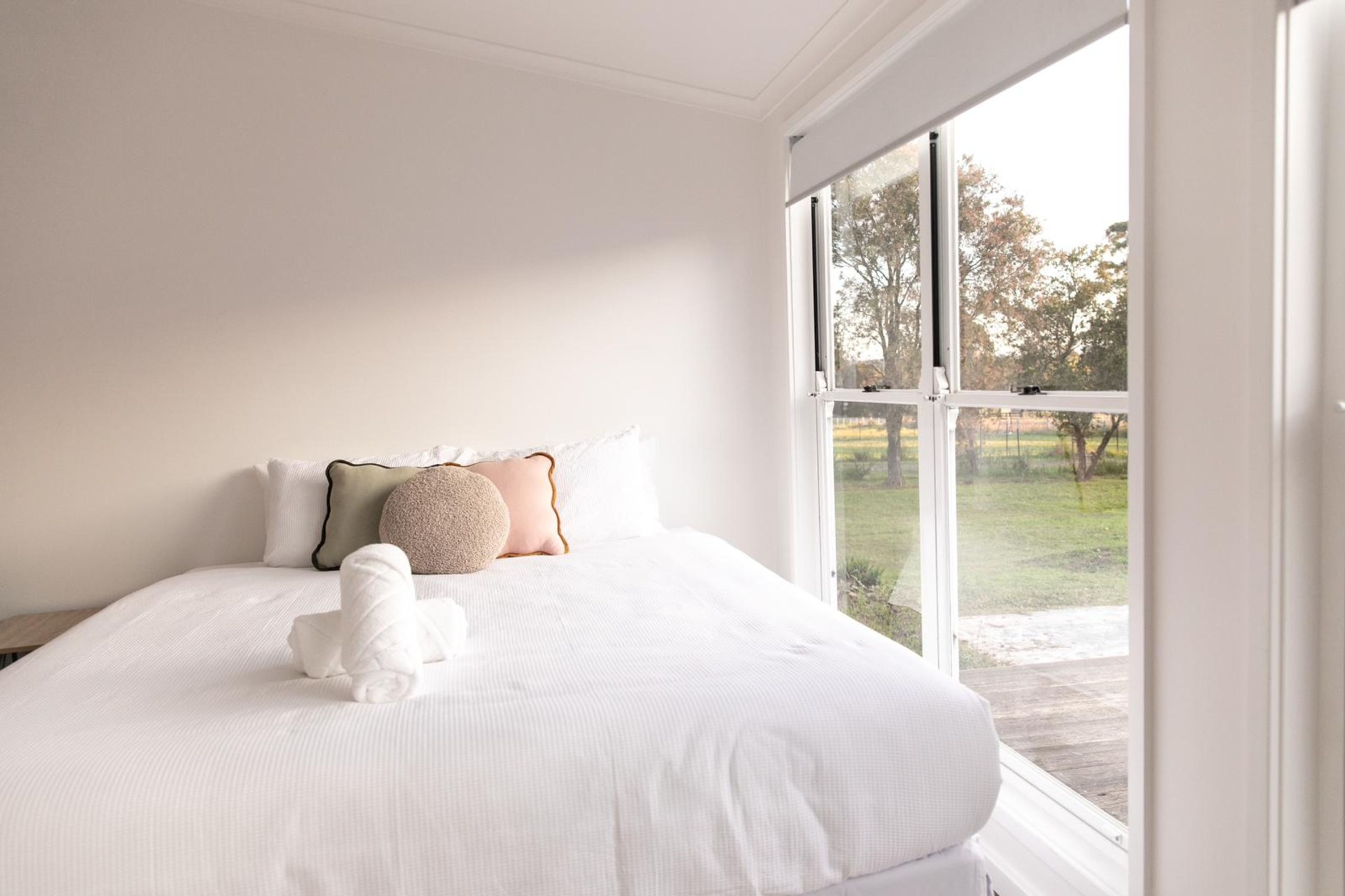 A bedroom with a large window, a bed with white bedding, and a small white dog.