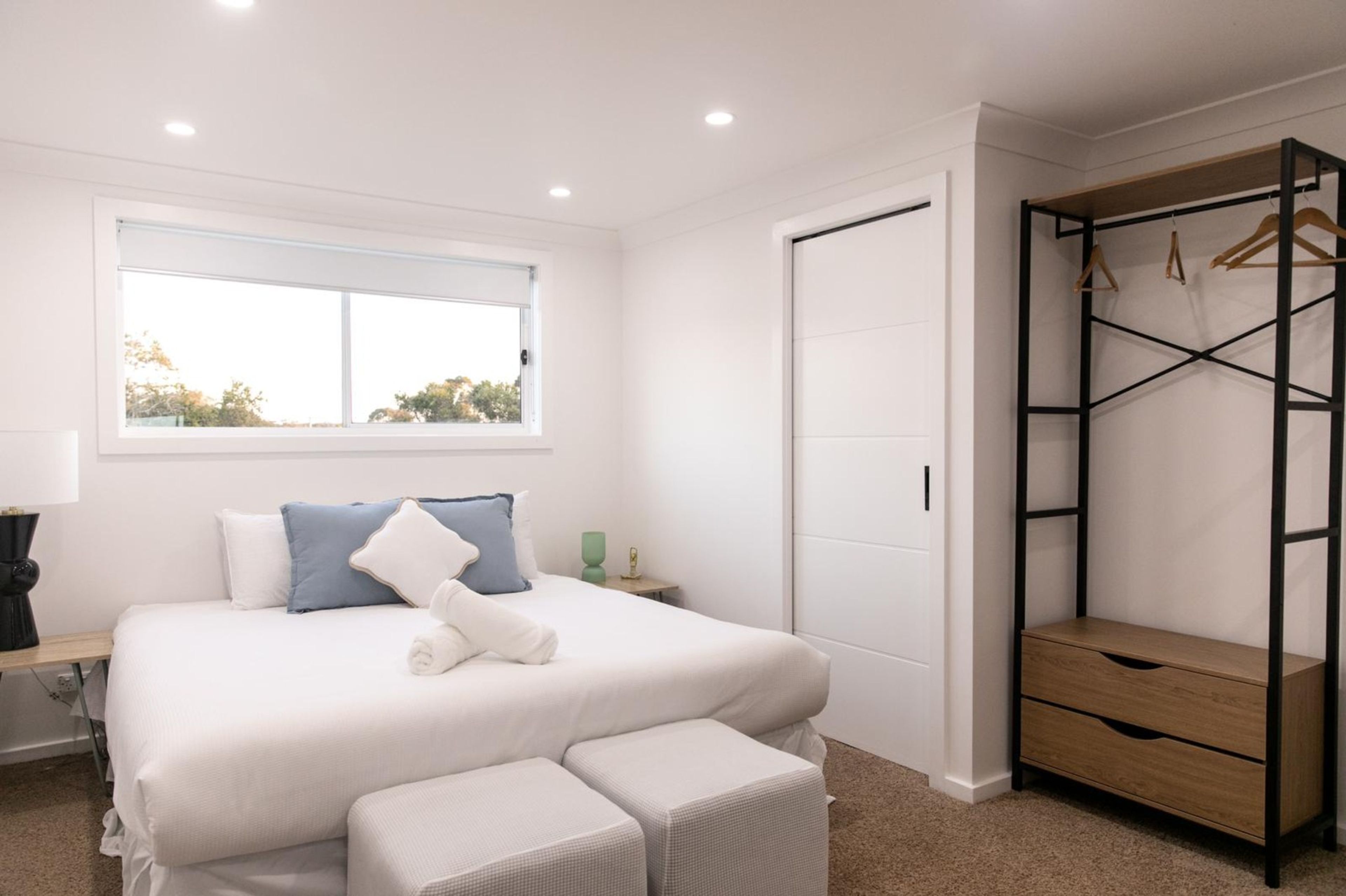 A bedroom with a bed, a bedside table, a lamp, a window, and a wardrobe.