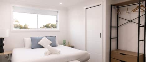 Un dormitorio con cama, mesita de noche, lámpara, ventana y armario.