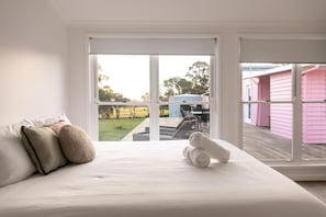 Un dormitorio con una cama grande, vistas a un jardín y un edificio rosa en el exterior.