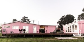 A pink mobile home with a porch, outdoor seating, and a small deck.