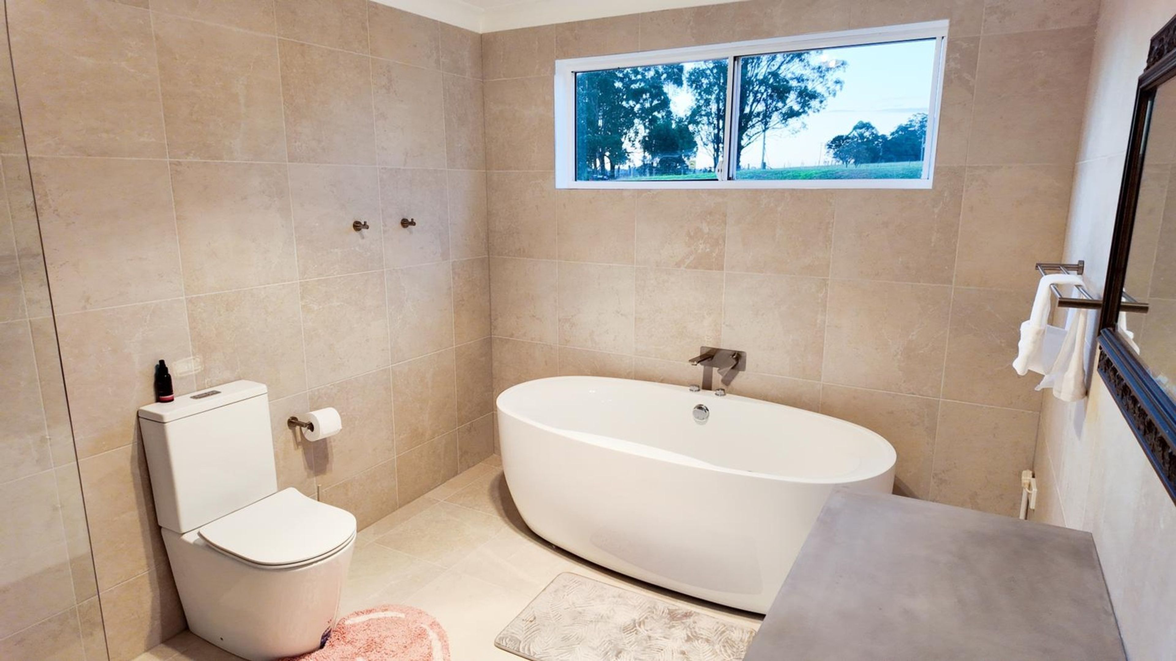 Ein Badezimmer mit Badewanne, Toilette und einem Fenster mit Blick auf Bäume.