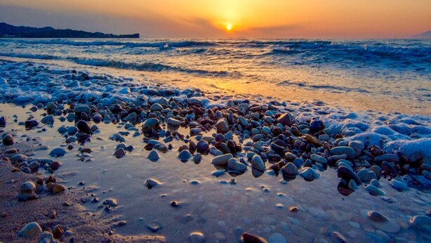 A beach with pebbles and the sun setting over the water. - Boutique Villa Elea with private pool (Acharavi)